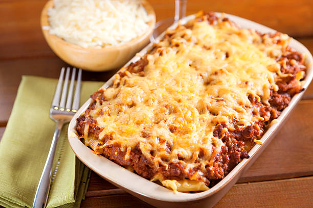 Baked lasagna topped with melted cheese served in a dish with a bowl of grated cheese in the background.