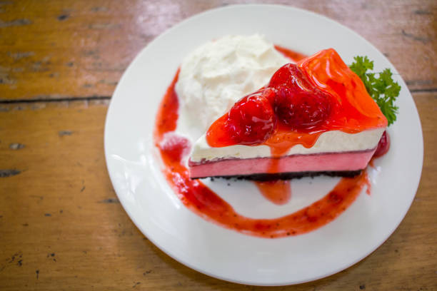 A slice of strawberry cheesecake on a white plate with whipped cream and a sauce drizzle.