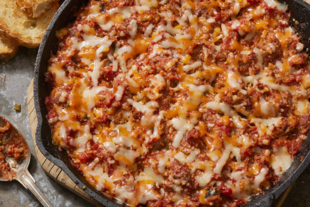 A close-up view of a savory baked dish in a cast iron skillet, featuring a mixture of ground meat, cheese, and tomato sauce topped with melted cheese.