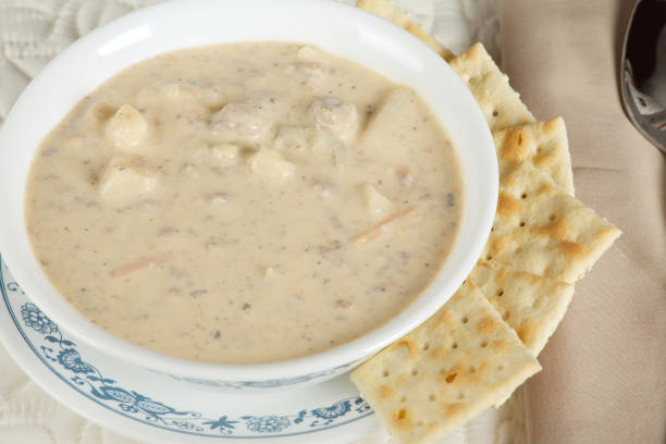 A bowl of creamy soup with chunks of vegetables and meat, accompanied by crackers on a plate.