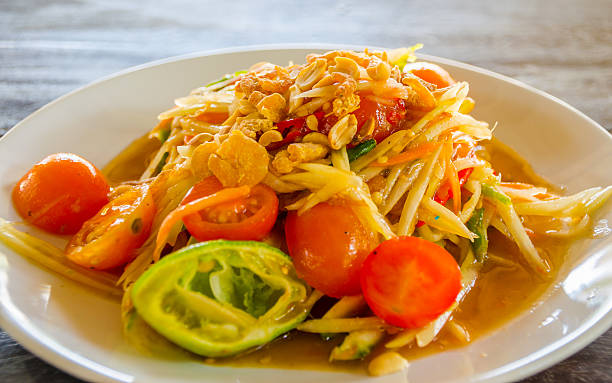 A vibrant plate of papaya salad with tomatoes, peanuts, and lime slices garnished on top.