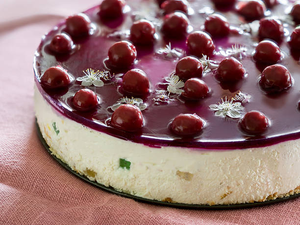 A beautifully presented cheesecake topped with cherries and edible flowers on a soft pink cloth.