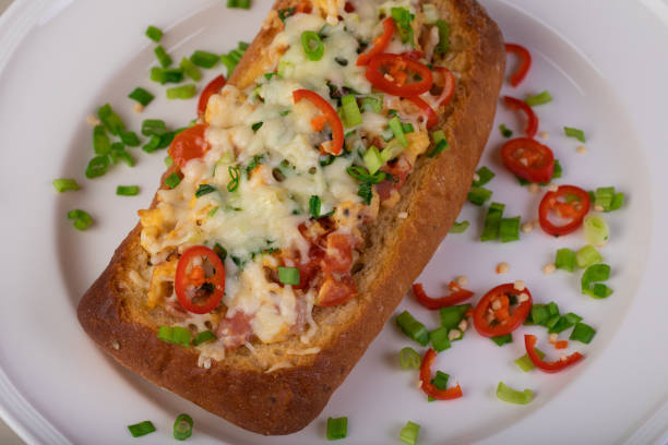 A delicious baked dish made from a bread roll topped with cheese, tomatoes, red chili slices, and green onions, served on a white plate.