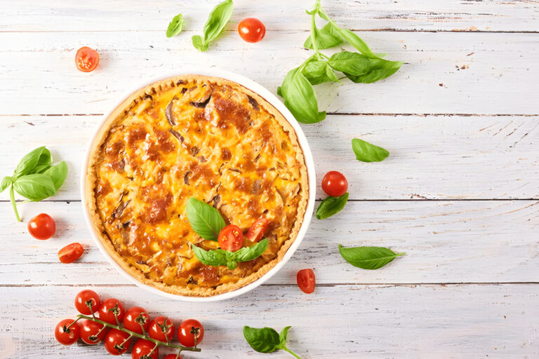 Delicious baked pie with a golden crust, topped with melted cheese and garnished with fresh basil and cherry tomatoes, on a rustic wooden surface.