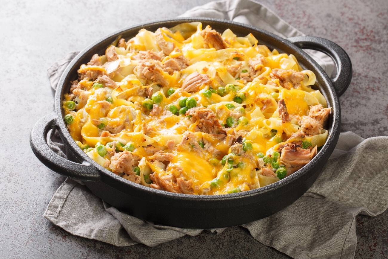 A baked noodle dish with shredded chicken, peas, and melted cheddar cheese in a black serving dish.