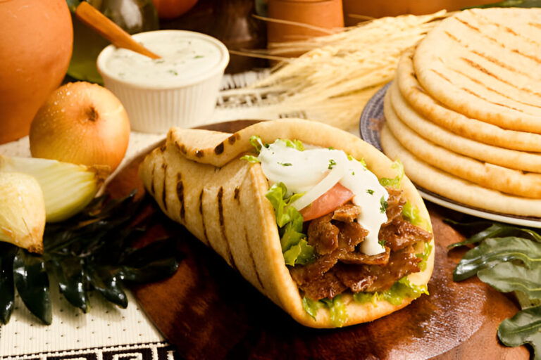 A freshly made wrap filled with beef, lettuce, tomato, onions, and a creamy sauce, served on a wooden platter with additional flatbreads and onions in the background.