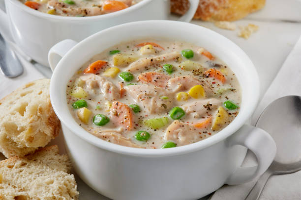 A bowl of creamy chicken soup with vegetables, served with bread on the side.