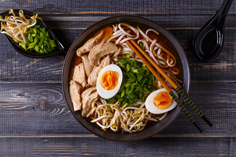 A bowl of ramen with chicken, egg, and green onions on a wooden surface.