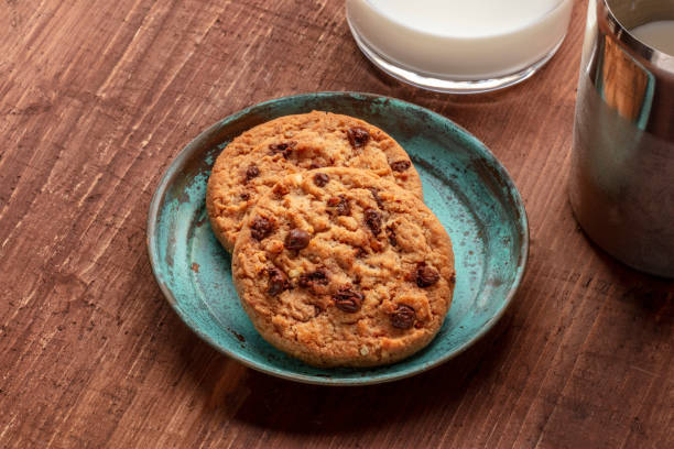 Two freshly baked cookies on a blue plate next to a glass of milk