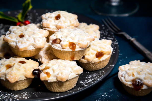 A festive plate of mini pies topped with powdered sugar and fruit preserves, surrounded by decorative holly and a vintage fork.