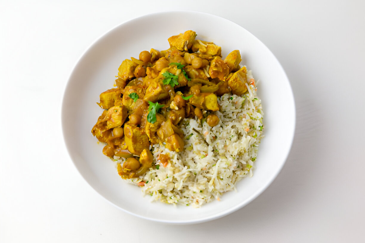 A bowl of curry with chicken and chickpeas served alongside a portion of fluffy rice, garnished with cilantro.