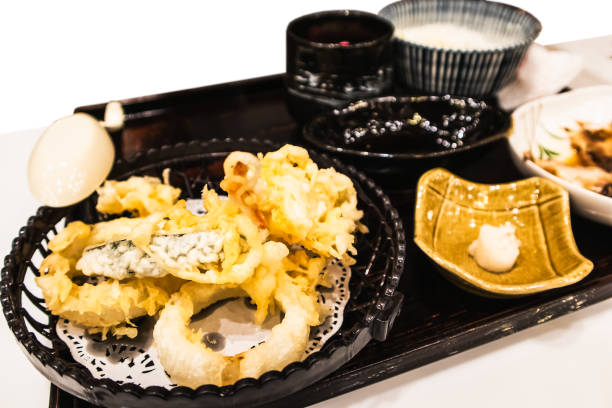 A beautifully arranged Japanese tempura dish served on a black platter, featuring various tempura vegetables and seafood with dipping sauces.