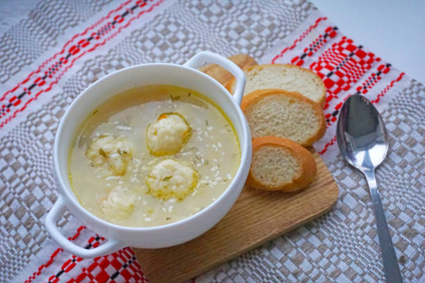 A bowl of soup with dumplings, served with slices of bread on a wooden board.