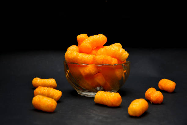 Bowl of bright orange cheese puffs on a black background.