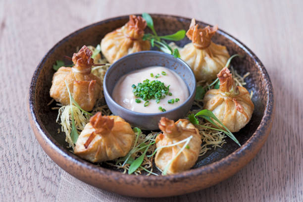 A plate of delicately prepared dumplings served with a creamy dipping sauce and garnished with green herbs.