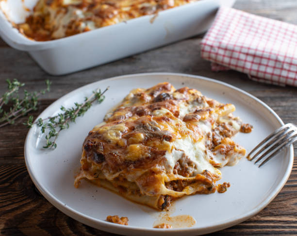 A serving of lasagna on a white plate with herbs on a wooden surface.