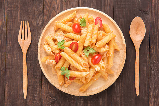 A wooden plate filled with pasta and cherry tomatoes garnished with green herbs, surrounded by wooden cutlery.