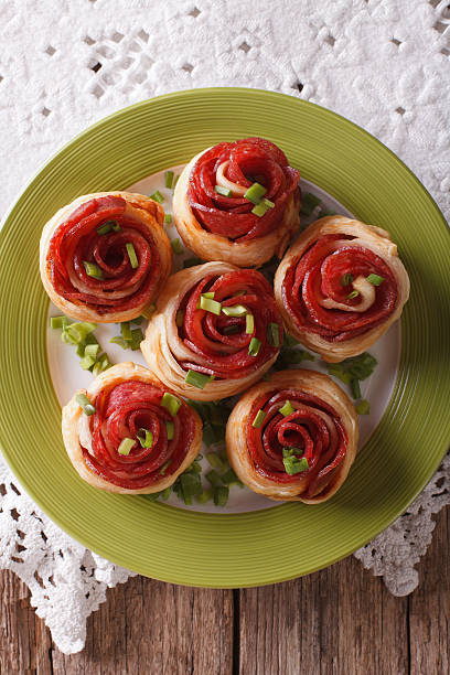 A plate of six pastry rolls resembling roses, topped with green onions.