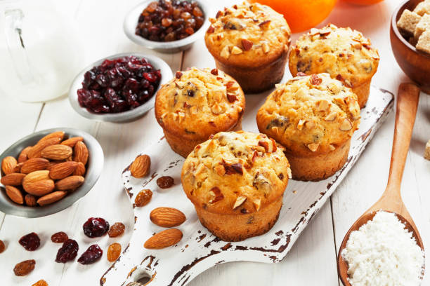 Freshly baked muffins topped with nuts and surrounded by various ingredients including almonds, dried fruits, and sugar.