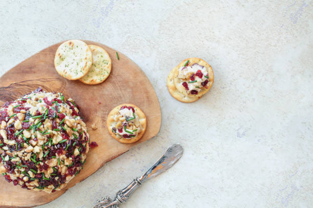 A wooden board displaying a cheese ball topped with nuts and cranberries, surrounded by crackers and a decorative knife.