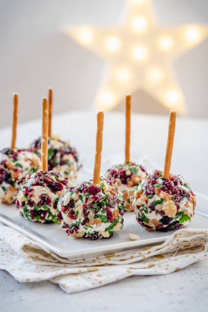 Colorful cheese balls coated with nuts and herbs on skewers, arranged on a plate with a star-shaped light in the background.