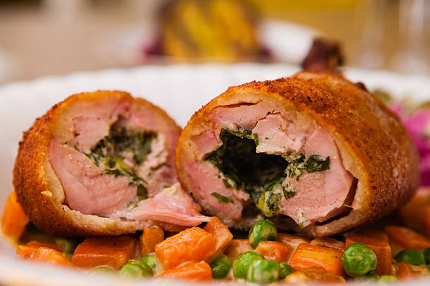 A close-up view of a halved breaded meat dish filled with greens, served on a plate with a mix of vegetables.