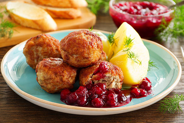 A plate of meatballs served with potato wedges and cranberry sauce.