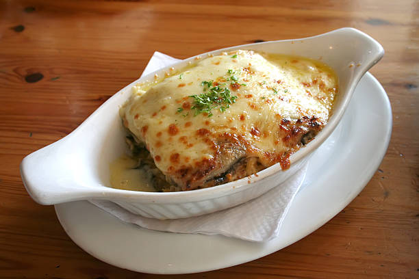 A serving of baked lasagna topped with melted cheese and garnished with herbs, served in a white dish.