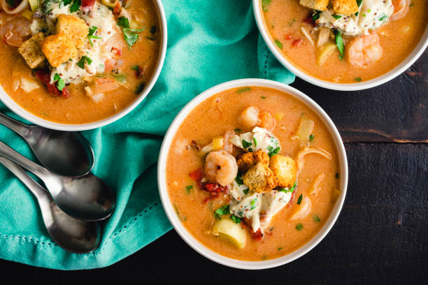 Three bowls of creamy shrimp soup topped with croutons and herbs, served on a teal cloth.