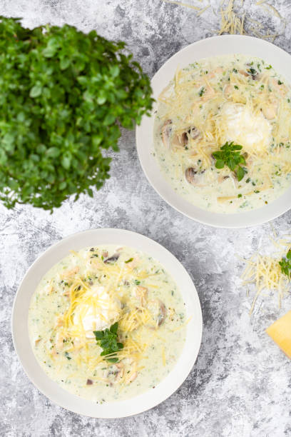 Two bowls of creamy soup topped with cheese and herbs, with a potted plant in the background.