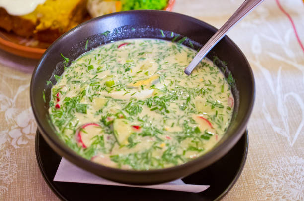 A bowl of creamy green soup with herbs, sliced vegetables, and a spoon