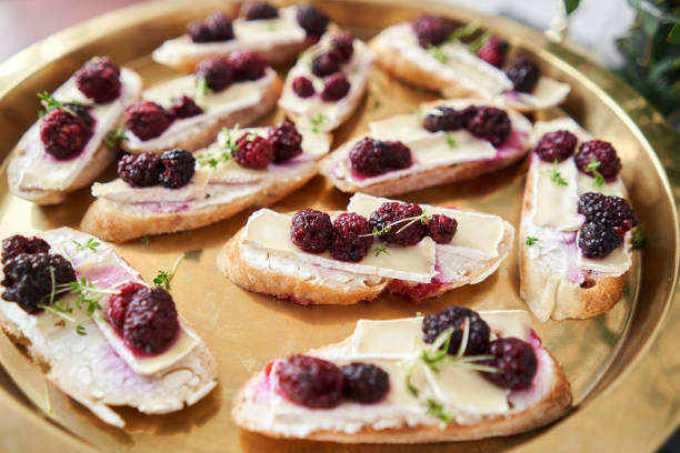 A platter of bruschetta topped with cheese and blackberries arranged on a gold tray.