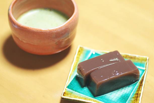 A plate with a brown jelly dessert next to a traditional tea cup filled with green tea.