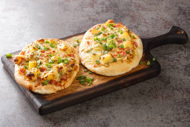 Two delicious mini pizzas topped with cheese, pineapple, and green onions, served on a wooden cutting board.