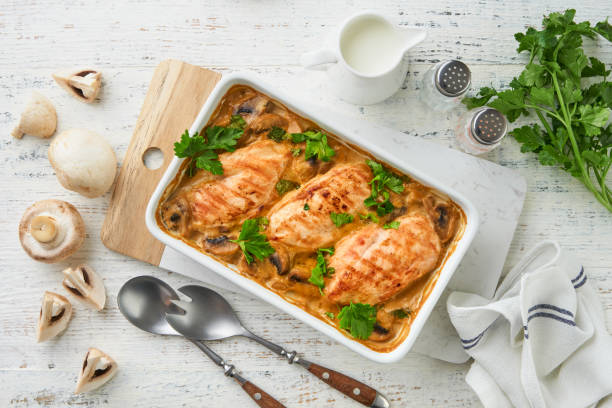 Baked chicken breasts in a creamy mushroom sauce garnished with parsley, surrounded by cooking utensils and fresh ingredients.