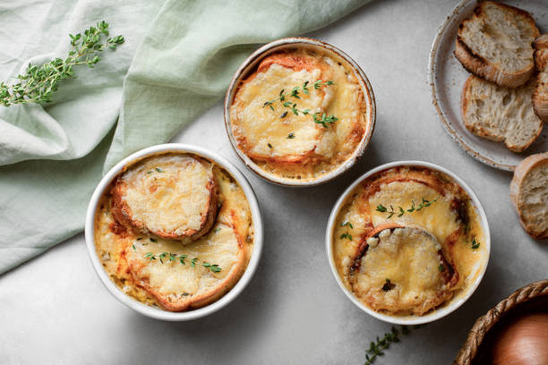 Three bowls of French onion soup with toasted bread and melted cheese, garnished with fresh thyme, on a light gray surface.