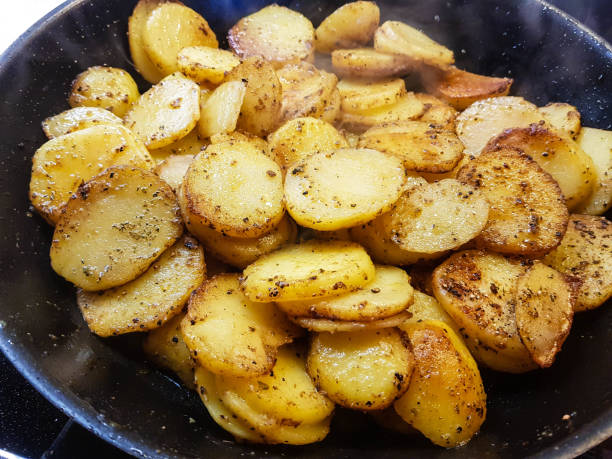 A close-up of golden-brown, sautéed sliced potatoes in a frying pan.