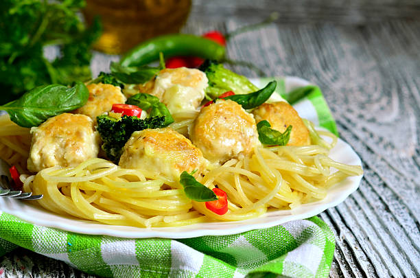 A plate of spaghetti with meatballs garnished with basil and red chili on a checkered cloth.