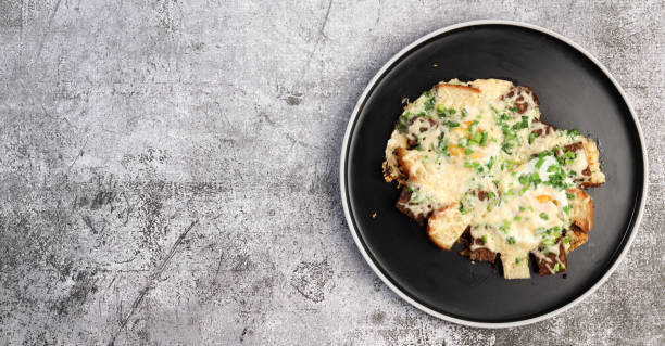 A plate of cheesy baked dish topped with herbs on a textured gray background.