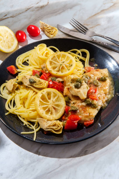 Plate of chicken piccata served with pasta, garnished with lemon slices and cherry tomatoes.