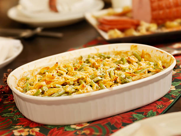 A creamy green bean casserole topped with melted cheese in a white baking dish on a festive table.