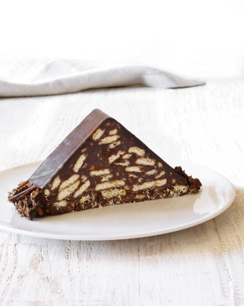 A triangular slice of chocolate biscuit cake on a white plate against a light background.