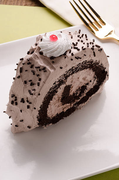 Slice of chocolate roll cake topped with whipped cream and a red cherry