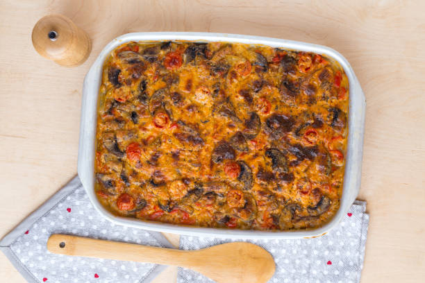 A delicious baked casserole with a golden, cheesy top and red tomatoes, placed in a white dish on a wooden table.