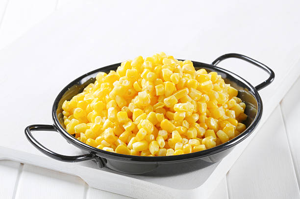 A black serving dish filled with yellow corn kernels on a white cutting board