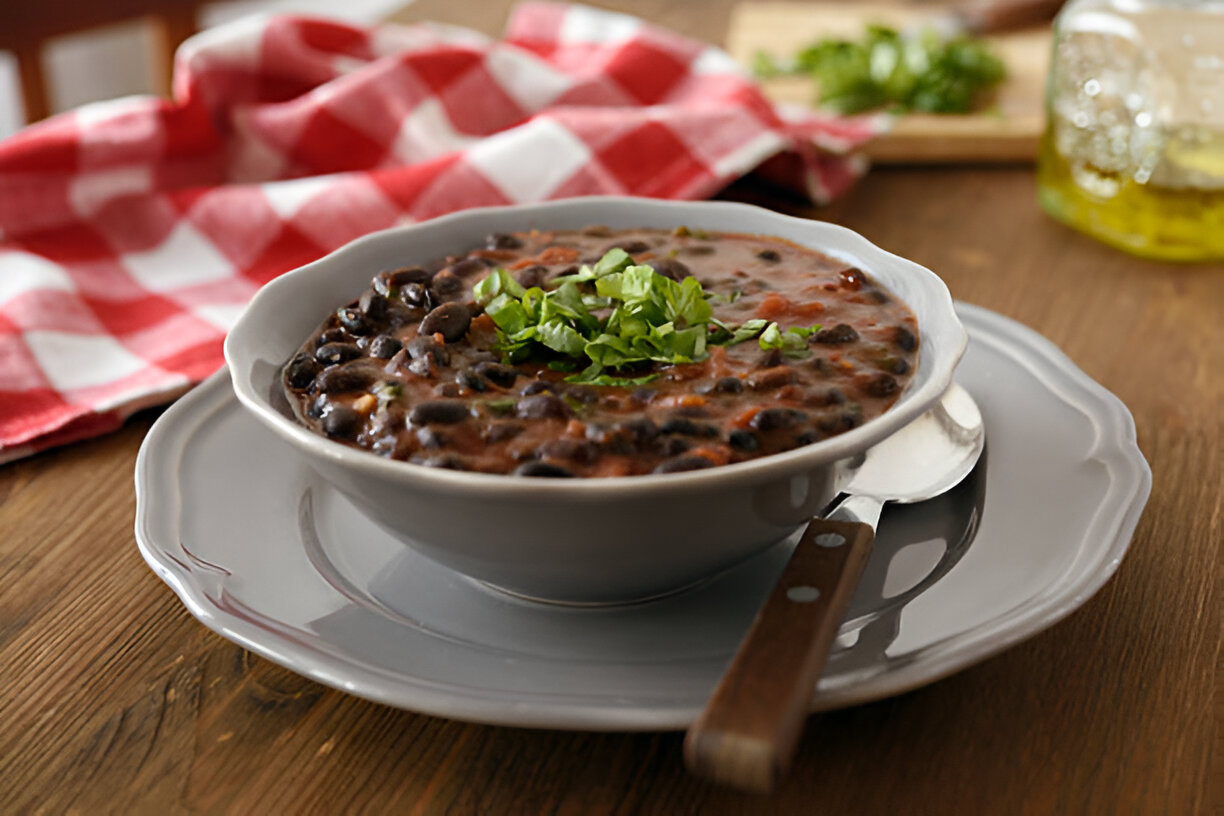 A bowl of black bean soup topped with chopped cilantro, placed on a gray plate with a spoon.