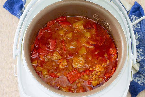 A close-up view of a delicious stew cooking in a rice cooker, featuring chunks of meat, red and yellow bell peppers, and various vegetables in a rich sauce.