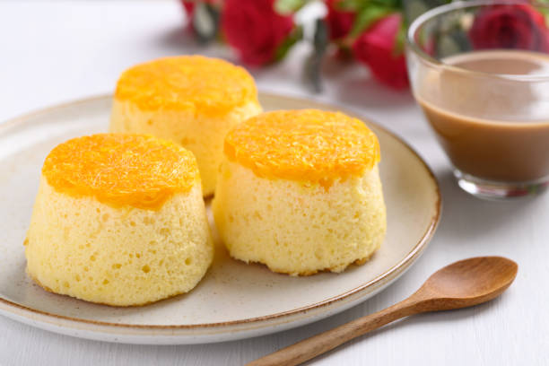 Three vibrant yellow desserts on a white plate, accompanied by a glass of coffee and a wooden spoon.