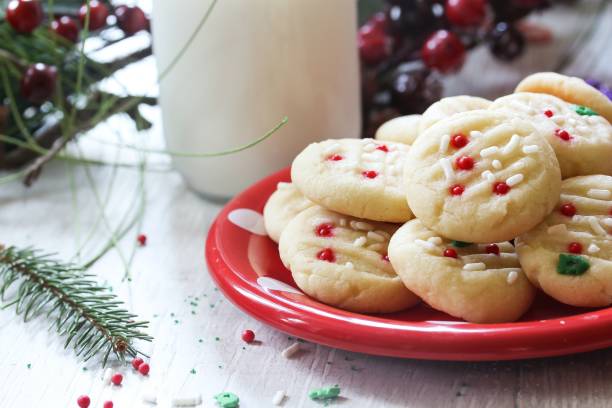 A platter of festive cookies with red and green decorations beside a glass of milk and holiday decorations.