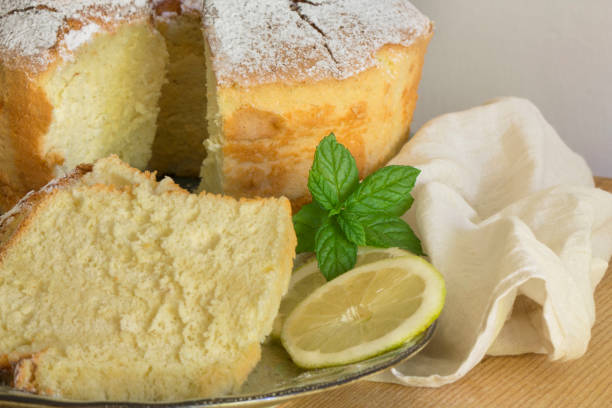 A slice of lemon cake displayed with fresh mint leaves and lemon slices on a wooden surface.